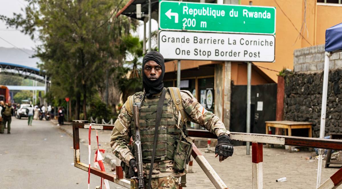 M23 rebel fighter A member of the M23 rebel group stands at a road barrier, with a sign behind him pointing to the Rwanda border.
